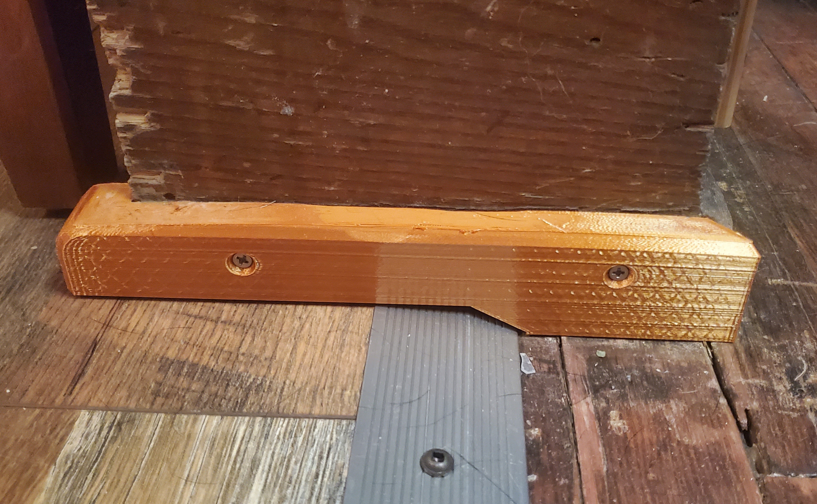 A 3D printed border for a piece of woodwork between uneven sections of flooring.